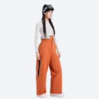 
                  
                    Women's colorblock snowboard jacket with wide-leg pants - orange wide-leg snow pants with white top, on-model side view
                  
                