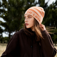 
                  
                    Fine 17.5 micron merino wool beanie - orange letter print merino beanie on women, worn side view, for winter mountain trips
                  
                