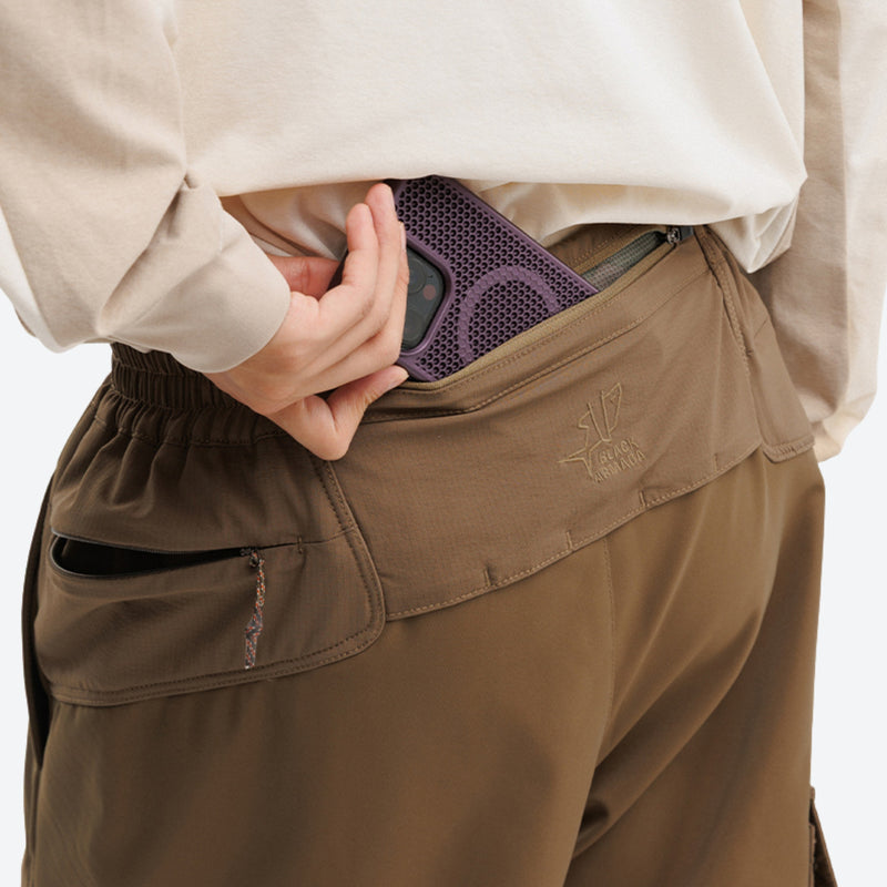 Unisex lightweight softshell outdoor pants - tan, waist pocket close-up with hand and phone, for skiing and snowboarding