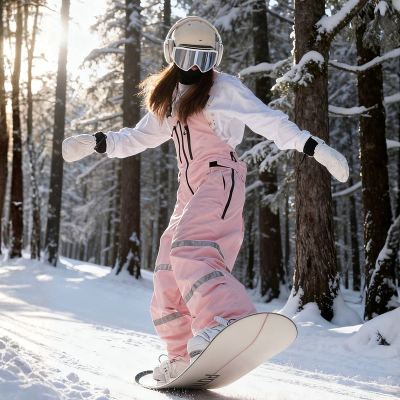 Unisex snowboard bib pants - pink bib pants with black top, riding snowboard on snowy slope, for cold-weather winter sports