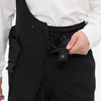 
                  
                    Unisex waterproof 3L bib snow pants - black, chest snap close-up with hand, for resort and backcountry days
                  
                