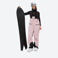 
                  
                    Insulated bib snow pants for women - pink bib pants, on-model front with upright snowboard, for cold-weather winter sports
                  
                