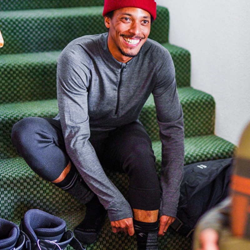 Men's 100% merino wool half-zip base layer top - gray merino wool half-zip top on men with red beanie, sitting view on stairs
