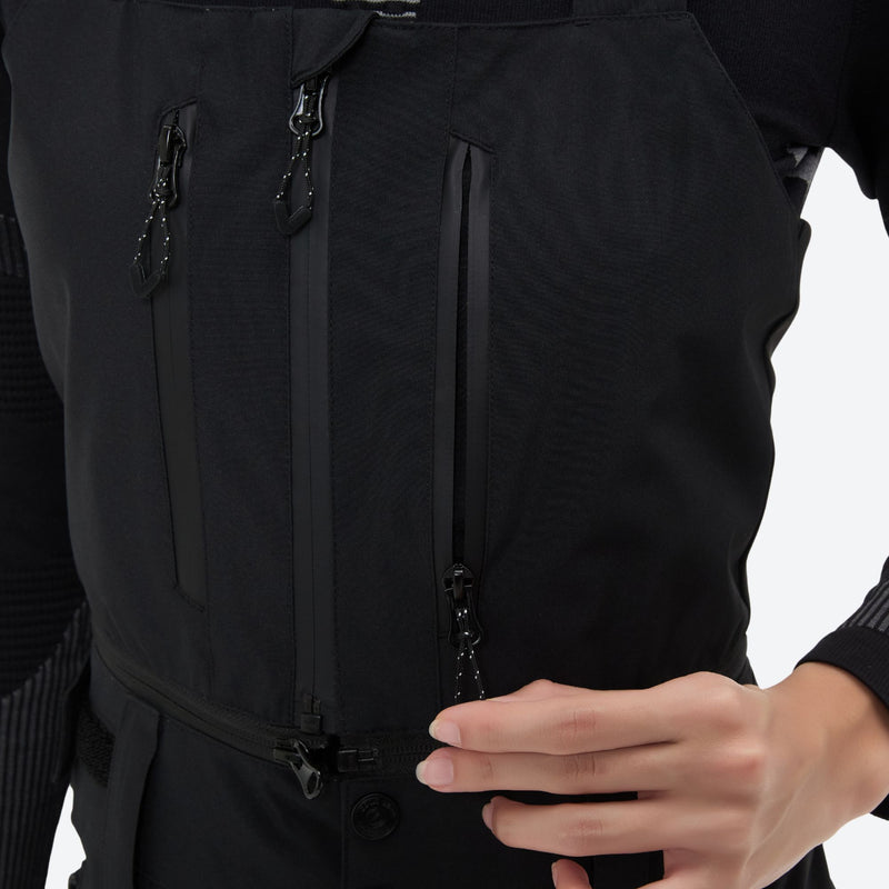 Breathable 3-layer ski bibs with cross-back straps - black, chest zip close-up with hand, for powder and piste riding