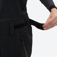 
                  
                    Unisex snowboard bib pants with snow gaiters - black, waist belt strap close-up with hand, for powder and piste riding
                  
                
