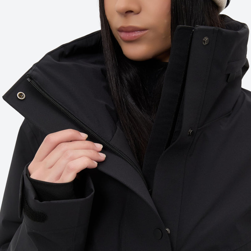Women's belted snow jacket with suspender pants - black, collar close-up with hand, for cold-weather winter sports