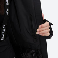 
                  
                    Women's belted snow jacket with suspender pants - black, chest zip close-up with hand, for resort and cross-country days
                  
                
