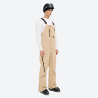 
                  
                    Men's waterproof 3L bib snow pants - tan bib snow pants with white top, on-model side view, for cold-weather winter sports
                  
                