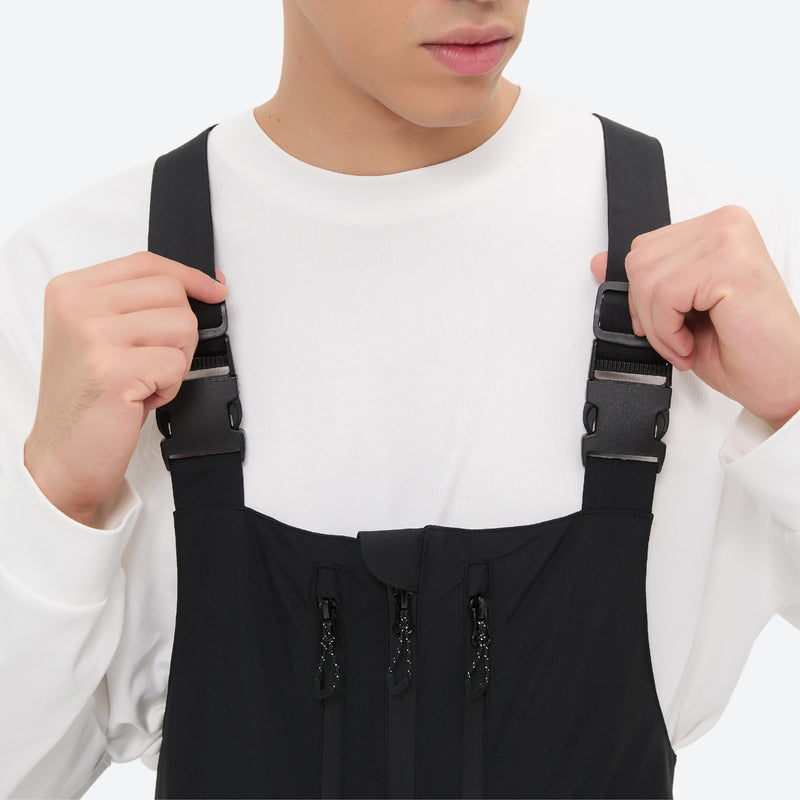 Unisex waterproof 3L bib snow pants - black bib pants, suspender strap close-up with hand, for powder days and winter commute
