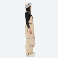 
                  
                    Women's waterproof 2L snow jacket and bib pants series - tan bib pants, on-model side view, for resort and street wear
                  
                