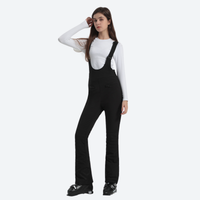 
                  
                    Women's slim fit waterproof ski bib pants - black slim fit ski bib, front view with hand at cap, for resort ski days
                  
                